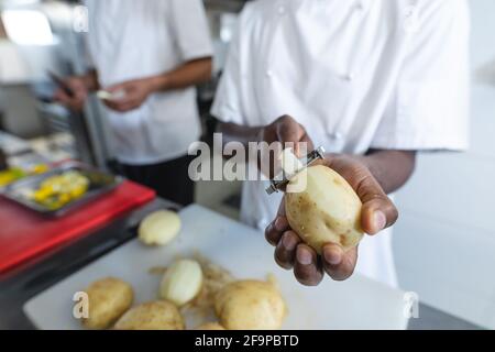 Midsection of diverce race professional chefs preparing vegetables wearing. working in a busy restaurant kitchen. Stock Photo