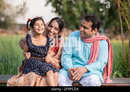 Happy Indian farmer family at agricultural field in village, Young couple with their daughter in traditional outfit. Stock Photo
