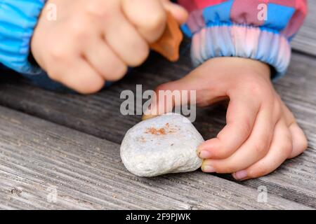 Close-up of the hands of  4 year old child holding  stones in her hands and hitting them on each other outdoors on a wooden ground. Seen in Germany in Stock Photo