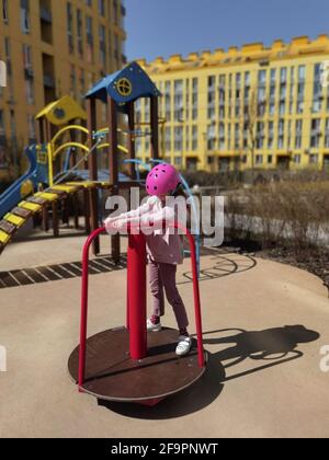 A girl of eight years in crash helmet riding on carousel. Child on merry-go-round Stock Photo