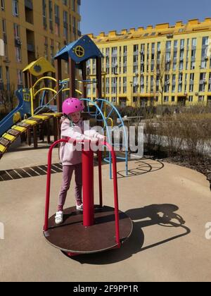 A girl of eight years in crash helmet riding on carousel. Child on merry-go-round Stock Photo