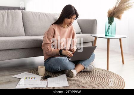 Focused woman working on laptop sitting on floor at home Stock Photo