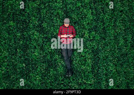 Drone operator, top view of man lying in grass field and using drone remote controller, copy space included Stock Photo