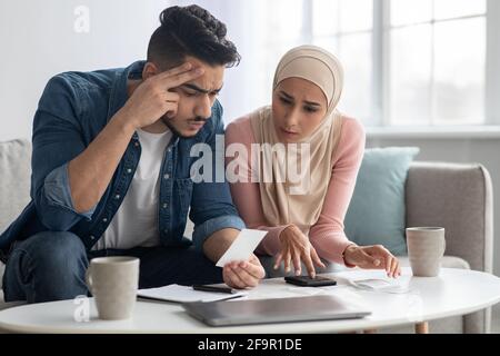 Confusded lady in hijab and her upset husband with bills Stock Photo