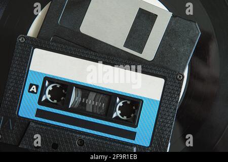 On the vinyl record are a black audio cassette and a floppy disk. Top view. Close-up Stock Photo