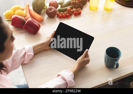 Woman using tablet with empty screen for mockup in kitchen Stock Photo