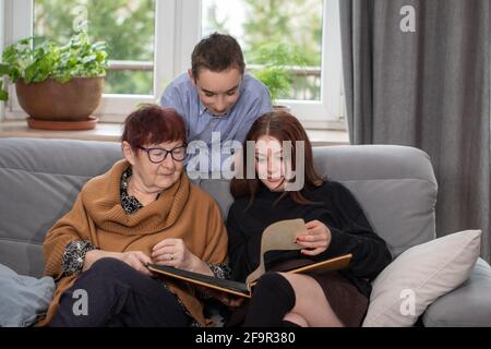 Multigenerational family, Smiling Family Watching into Photo Album on Sofa. Grandmother and grandchildren watching old photo album at home. Stock Photo