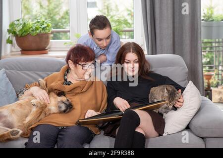 Multigenerational family, Smiling Family Watching into Photo Album on Sofa. Grandmother and grandchildren watching old photo album at home. Stock Photo