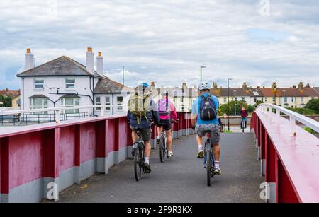 Small group of cyclists riding bicycles across a bridge. Cycling across a footbridge in England, UK. Stock Photo