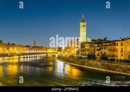 Beautiful view of colorful facades of old houses and Santa Anastasia churchon waterfront of the Adige River during night in Verona, Italy. Stock Photo