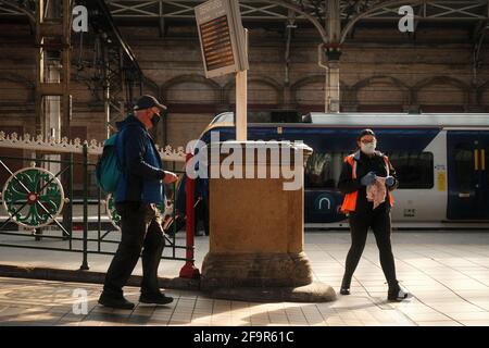 A passenger walking onto Preston Railway Station passing a member of staff with cleaning products, both wearing face masks. Stock Photo