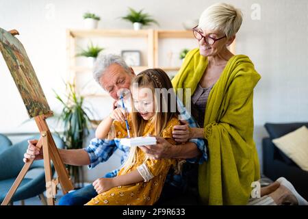 Senior people with child painting on canvas. Grandparents spending happy time with grandchild. Stock Photo