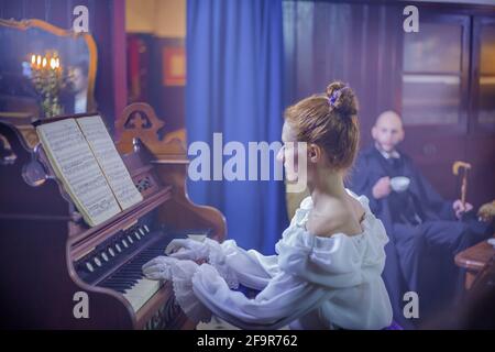 LUKOVICA, SLOVENIA - Apr 03, 2017: Young couple in vintage living room, woman plays piano, man enjoys her performance Stock Photo