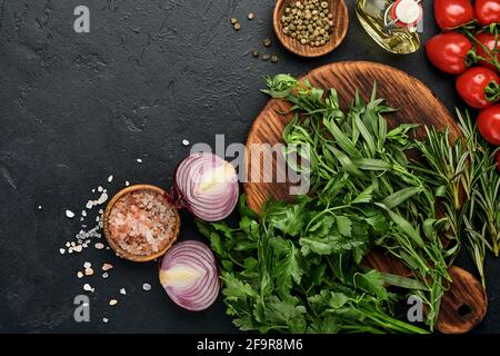 Fresh tarragon. Branch of fresh herb seasoning and cooking products, tomatoes, peppers, onions and olive oil on black concrete background. Cooking Bac Stock Photo