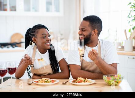 Domestic Lunch. Happy Black Spouses Eating Spaghetti And Drinking Wine In Kitchen Stock Photo