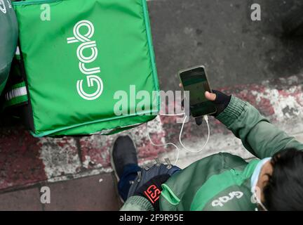 Bangkok, Thailand. 20th Apr, 2021. A Grab motorcycle rider checks his mobile phone.During the Covid-19 pandemic the Grab home food delivery service network has expanded with thousands of former motorcycle taxi riders nationwide changing to the Grab delivery service via the online Grab App. Customers can order their favorite Thai and western foods online from a variety of local and popular restaurants in Bangkok. (Photo by Paul Lakatos/SOPA Images/Sipa USA) Credit: Sipa USA/Alamy Live News Stock Photo