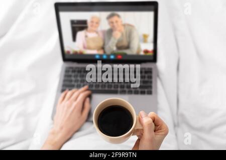 Unrecognizable Female Drinking Coffee In Bed And Making Video Call To Parents Stock Photo