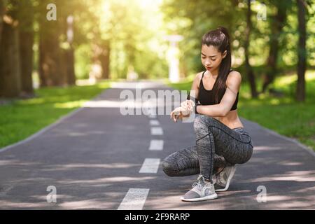 Beautiful asian girl taking break in running, using smartwatch to monitor progress Stock Photo
