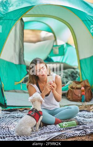 woman using her smartphone in the company of her dog outside her tent Stock Photo