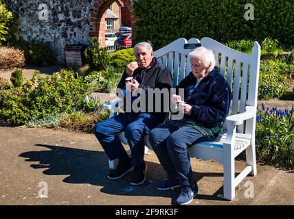 Elderly couple sitting on bench eating ice cream in sunshine, Lodge Grounds park, North Berwick, East Lothian, Scotland, UK Stock Photo