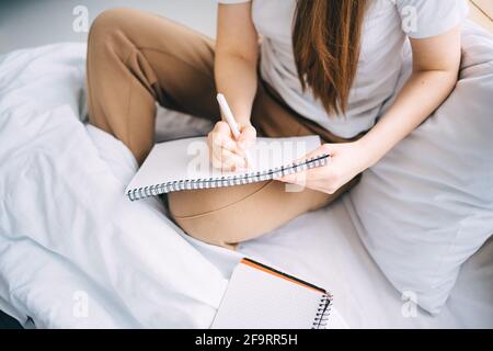girl writes in a notebook and listens to music in bed Stock Photo