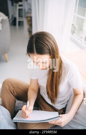 girl writes in a notebook and listens to music in bed Stock Photo