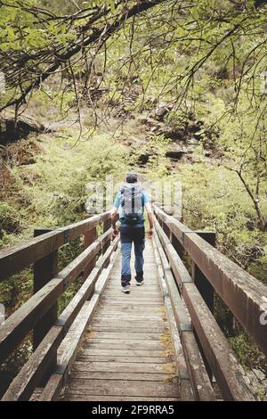 Man with backpack and cap crossing a bridge Stock Photo