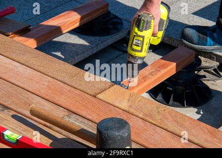 Hardwood terrace deck construction - builder hand with electric screwdriver close up view while installing exotic ipe wood decking lumber boards Stock Photo