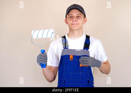 Master painter plasterer in overalls holds a roller in his hand. Blue jumpsuit with shoulder straps Stock Photo