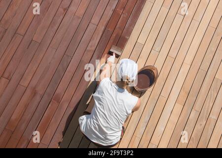 Hardwood deck oiling, decking renovation and nourishing by oil with a brush, overhead view of woman worker renovating wooden terrace Stock Photo