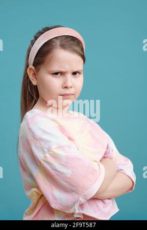 Portrait of little girl with angry face standing with arms crossed against the blue background Stock Photo