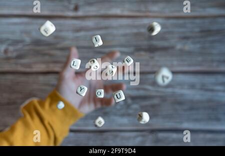 Selective focus on the dice. A hand throwing some dice in the air and the phrase "I love you" appears. Valentine's Day concept. Stock Photo