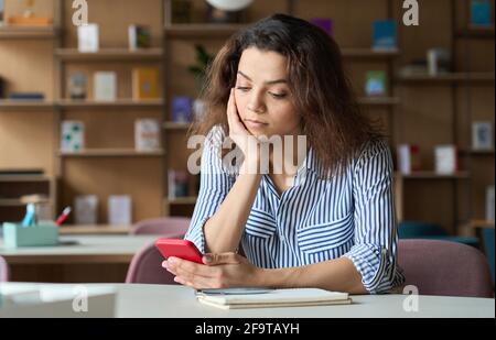 Indian student sitting at table with cellphone using training mobile app. Stock Photo