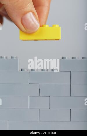 A yellow brick puts a hand on a toy gray wall. The concept of building, reaching and completing the goal Stock Photo