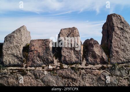 Stone wall rocks in front of blue sky with clouds Stock Photo