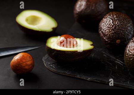Sliced and whole organic avocado Hass with a knife on a black background. A source of essential fats, vitamins, trace elements, beta-carotene and omeg Stock Photo
