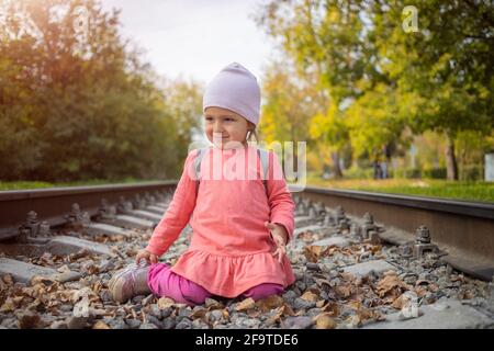 little girl sitting on the railroad tracks. toddler plays on railroad in forest Stock Photo