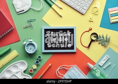 Zuruch in die Schule means or back to school in German language. Concept top view with chalk text on blackboard. Corona quick tests, mask, stationary Stock Photo