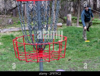 Selective focus of disc golf basket with middle aged man in background leaning over pick up his disc Stock Photo