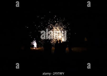 Group of people in silhouette watch colorful fireworks explode on a beach at night. Stock Photo