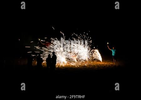 New Year’s Eve celebration on beach with fireworks on black background and people in silhouette. Stock Photo