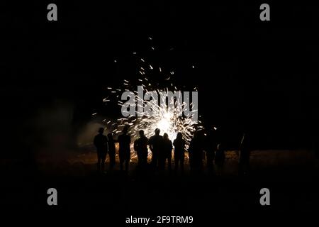 Group of people with backs turned in silhouette watch fireworks explode on beach at night. Stock Photo