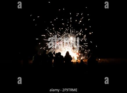 People take selfies and watch fireworks on beach with explosions of color against solid black night. Stock Photo