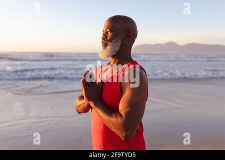 Senior african american man with folded hands meditating and practicing yoga at the beach Stock Photo