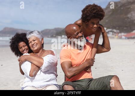 African american grandparents and grandchildren hugging while siting on the beach Stock Photo