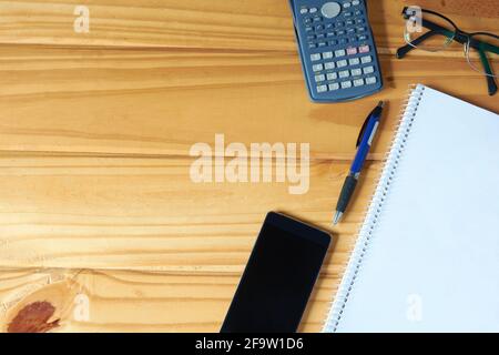 Top view of workplace with mobile phone, pen, blank notebook, calculator and glasses on rustic table. Copy space on the left. Stock Photo