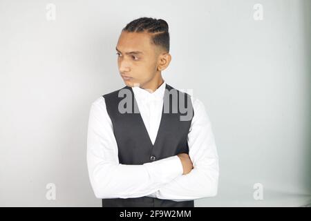 Serious young South Asian guy standing hands crossed wearing a white shirt and a vest Stock Photo
