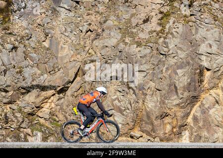 A man is riding a bike on a country road next to a rock wall in Coeur d'Alene, Idaho. Stock Photo