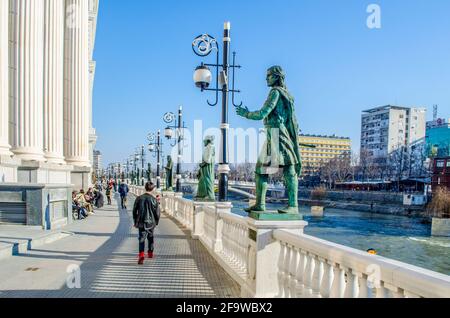 SKOPJE, MACEDONIA, FEBRUARY 16, 2015: people are walking through promenade decorated by many statues from archeological museum along vardar river in s Stock Photo