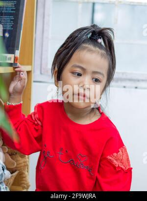 Vertical shot of a cute Southeast Asian baby girl staring with her big black eyes Stock Photo